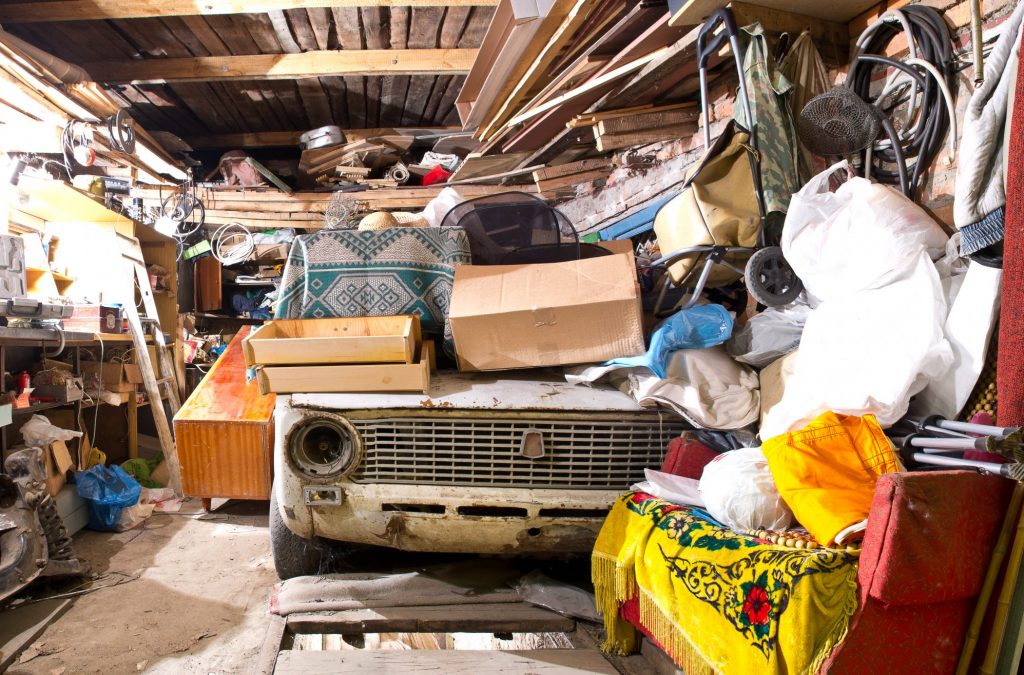 Garage inside. Old broken car, shelves with tools and stacks of things.